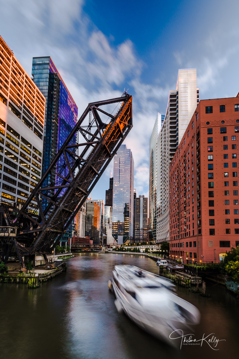 A long exposure of a river boat cruising along the Chicago River beneath the Kinzie Street Bridge.
